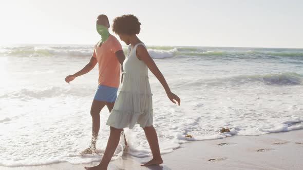 Smiling african american couple holding hands and walking on sunny beach