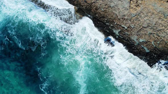 Sea Washes the Rocky Shore Above Aerial Shot Flying Over Coastline Cliffside with Blue Pure Water