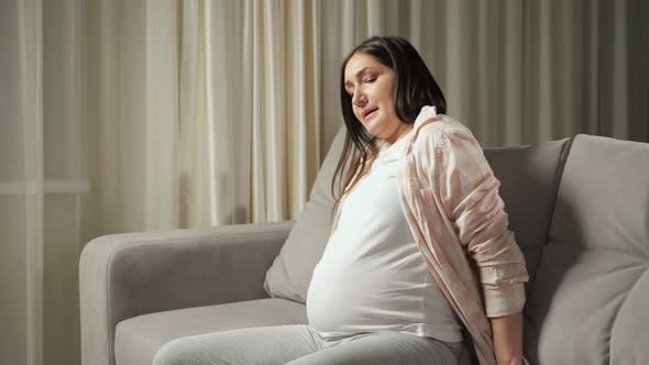 Pregnant Brunette Woman Struggles to Stand Up From Sofa