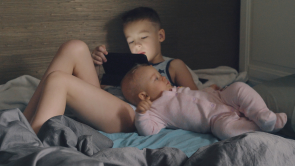 A Boy with a Tablet and His Baby Sister on a Messy Bed