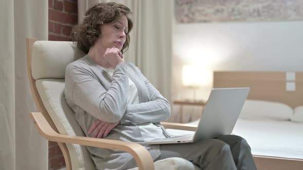 Old Woman Thinking and Working on Laptop on Sofa