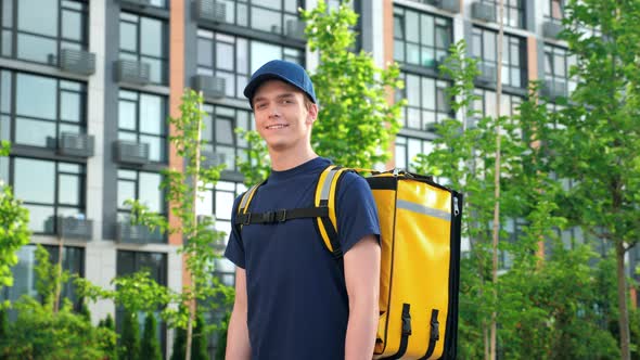 Positive Deliveryman Worker Wears Tshirt and Cap on Background Modern Building