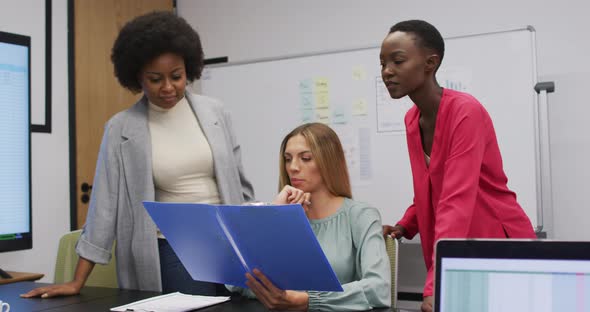 Three diverse businesswomen in discussion looking at paperwork in an office