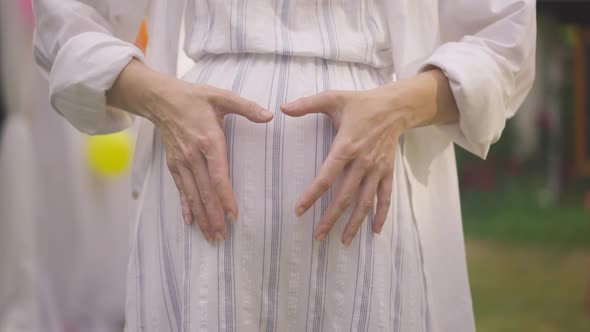 Closeup Female Hands Gesturing Heart Shape on Pregnant Belly in Slow Motion