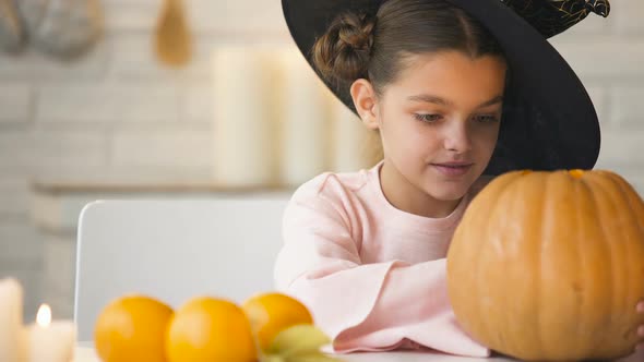 Cute Girl in Witch Costume Showing Jack Pumpkin and Smiling, Preparing for Party