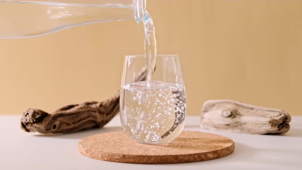 Pouring pure drinking water into a glass from a bottle on natural beige background