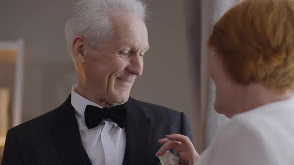 Closeup Portrait of Happy Senior Groom Smiling Looking at Bride As Woman Adjusting Boutonniere in