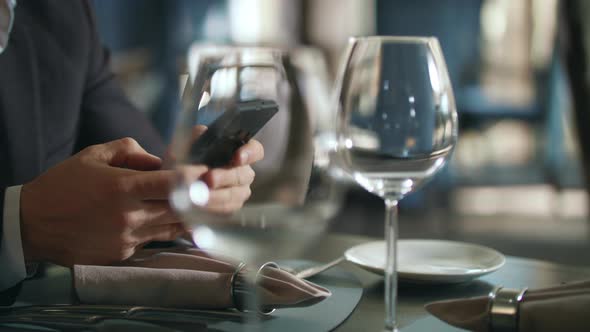 Male Hands Typing Phone at Restaurant Table. Businessman Using Smartphone