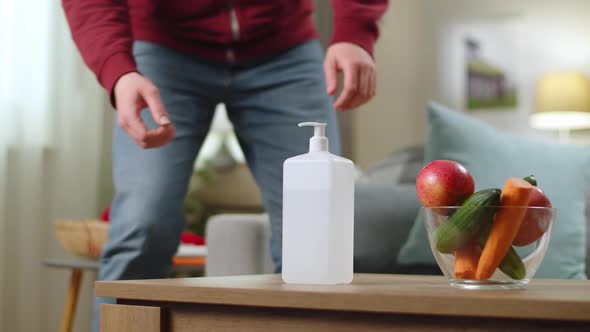 A Man Uses a Sanitizer to Disinfect the Hands at Home in the Living Room