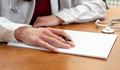 Female doctor hand with a pen on a blank paper, close up, wooden office table. - PhotoDune Item for Sale