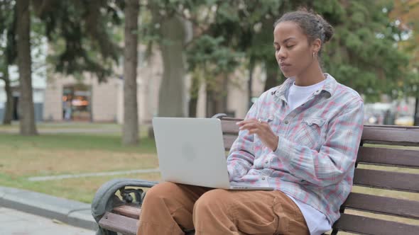 African Woman with Neck Pain Using Laptop While Sitting Outdoor on Bench