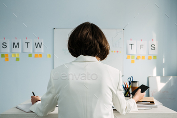 ness Owners managers. Young Businesswoman, manager standing in office in front of weekly schedule and sticking notes on wall