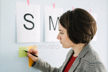 ness Owners managers. Young Businesswoman, manager standing in office in front of weekly schedule and sticking notes on wall