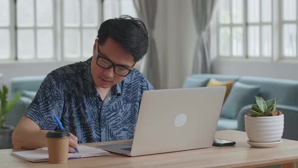 Asian Man Working With Laptop Computer And Writing On Notebook