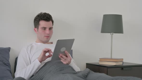 Man Reacting to Loss on Tablet While Sitting in Bed