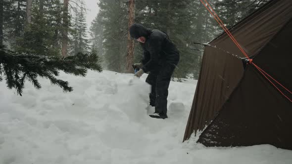 Shoveling snow on the edge of the tent. Surviving in the wild.