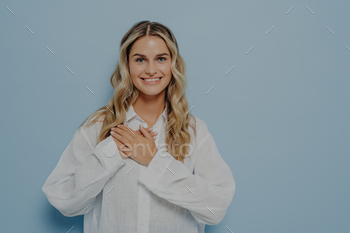 d with hands resting on her chest, standing relaxed and smiling, being grateful to whoever helped her, isolated in front of light blue background
