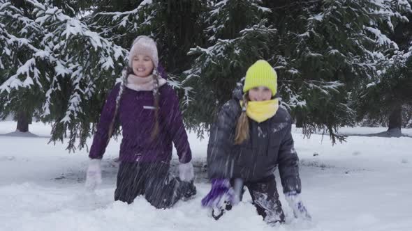 Two Teenage Girls Kneeling in the Snow and Having Fun Throwing Snowballs