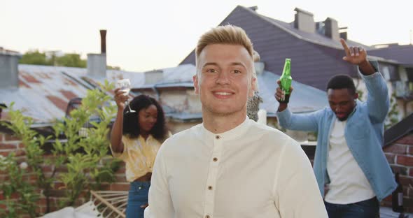 Guy Posing on Camera Near His Positive Mixed Race Dancing Friends on the Terrace