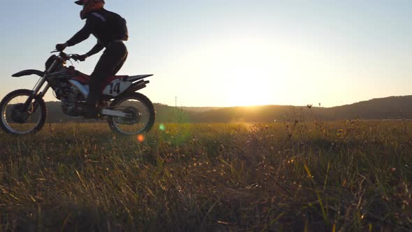 Two Motorcyclists Passing Through Field with Beautiful Sunset at Background. Warm Summer Sun Lights