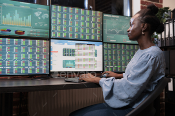 t multi monitor workstation while analyzing investment profits. African american business woman monitoring real time charts to foretell market trend.