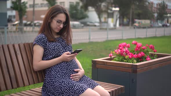 Young Pregnant Girl with a Phone in Her Hands
