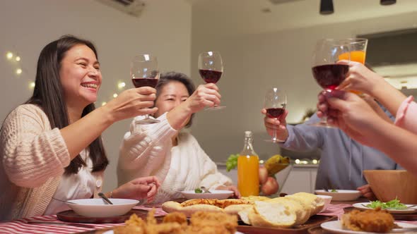 Asian big family having party eating food and toasting wine glass together on dining table at home.