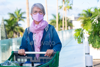 Caucasian senior woman wearing mask against coronavirus pushing the shoppping cart in the parking