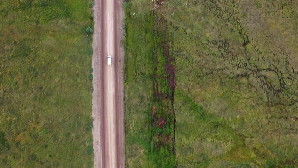 White minivan driving on a dirt road through Alaska grassy green wild terrains - aerial top-down tra