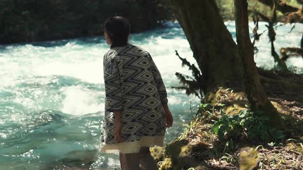 Glamorous Young Woman Is Walking Over River Shore in Forest and Sitting Down