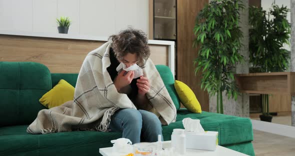 Young Sick Man Covered in Blanket Feeling Bad While Sitting on Sofa at Home