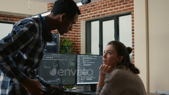 Junior developer sitting down on desk showing laptop with source code to senior dev