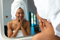 African american young woman wrapped in towel looking at her face in bathroom's mirror at home - PhotoDune Item for Sale
