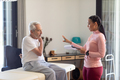 Biracial female physiotherapist with clipboard discussing with caucasian senior man at home - PhotoDune Item for Sale