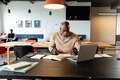 African american mature businessman writing in diary while sitting with at laptop in creative office - PhotoDune Item for Sale