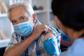 Biracial female health worker giving an injection to caucasian senior man at home - PhotoDune Item for Sale