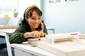 Asian young female architect talking on smart phone pointing at architectural model in office - PhotoDune Item for Sale