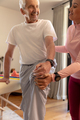 Biracial female physiotherapist helping caucasian senior man to stretch his leg at home - PhotoDune Item for Sale