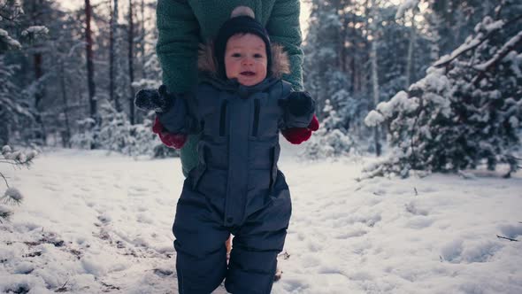 Mother Learning Her Little Baby Son His First Steps in the Snow Forest