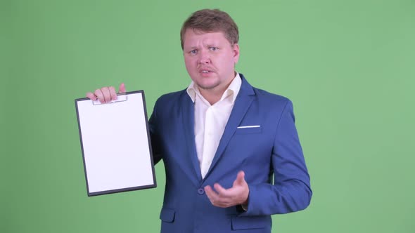 Stressed Overweight Bearded Businessman Showing Clipboard and Giving Thumbs Down