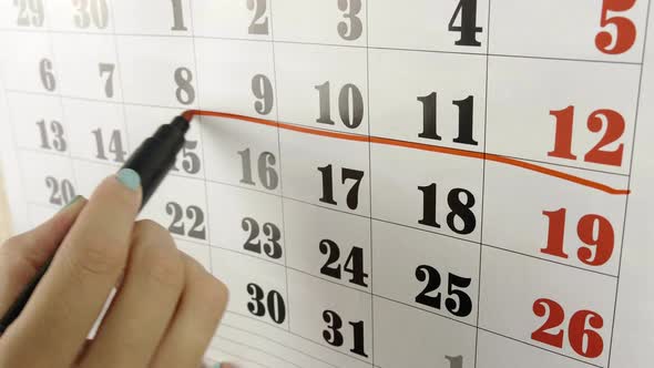 Female Hand Encircles with Red Marker the Calendar Week. Slow Motion Shot. Close Up