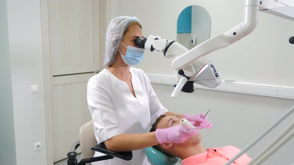 Female Dentist Treating Male Patient Using White Proffessional Microscope