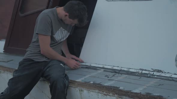 Young caucasian carpenter trimming excess sikaflex sealant on wooden boat trim