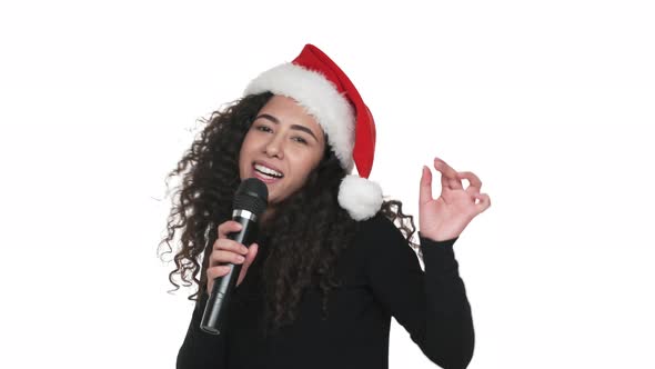 Portrait of Joyous Female Wearing Santa Claus Red Hat Celebrating Christmas Singing in Karaoke Using