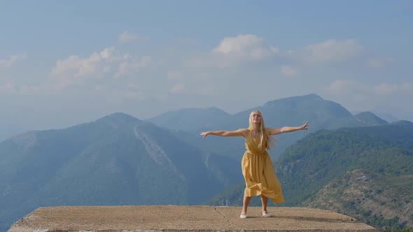 Dancing blonde woman in a yellow dress  against the background of mountains in Montenegro.