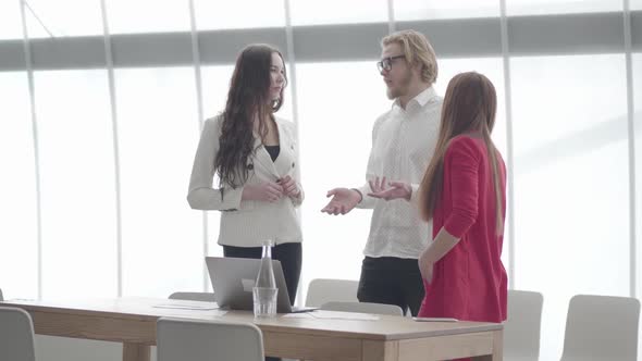 Businessman in Glasses Gesticulating While Explaining His Idea To Two Female Colleagues Standing in