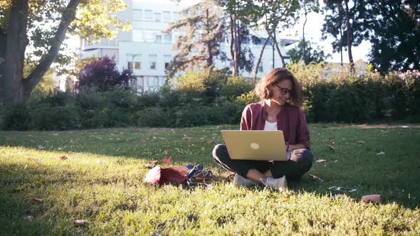 Young Girl Student Sitting on the Lawn in the Park with a Laptop and Smartphone