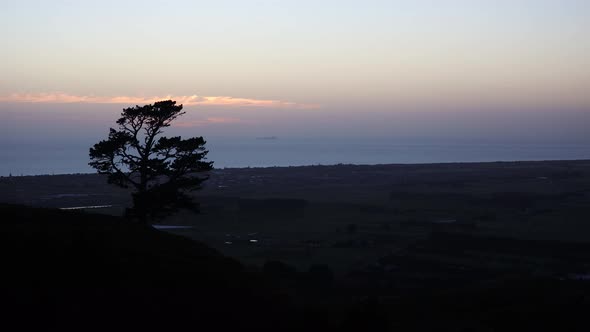 Wide sunrise time lapse of silhouette of tree with Papamoa town and beach in background. Shot from t