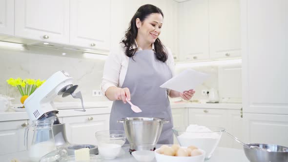 a Woman Cook with a Recipe Ingredients and a Mixer Prepares Pastries