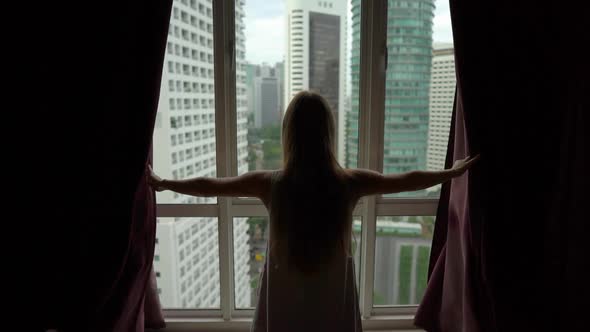 Superslowmotion Shot of Successful Rich Young Woman Opening Curtains in Her Downtown Apartment with